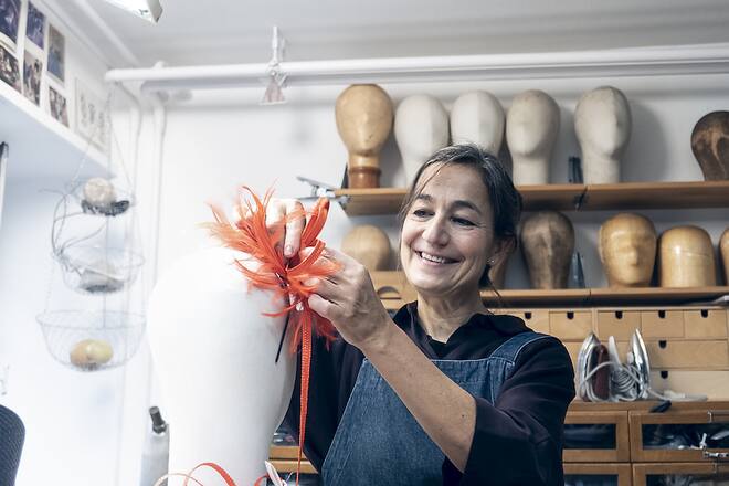 a woman in an atelier fixing feathers on a fake head