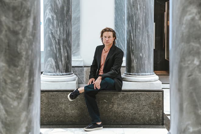a man with glasses sitting between columns