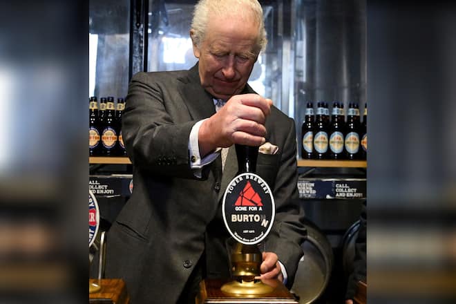 König Charles III. bedient sich am Zapfhahn.