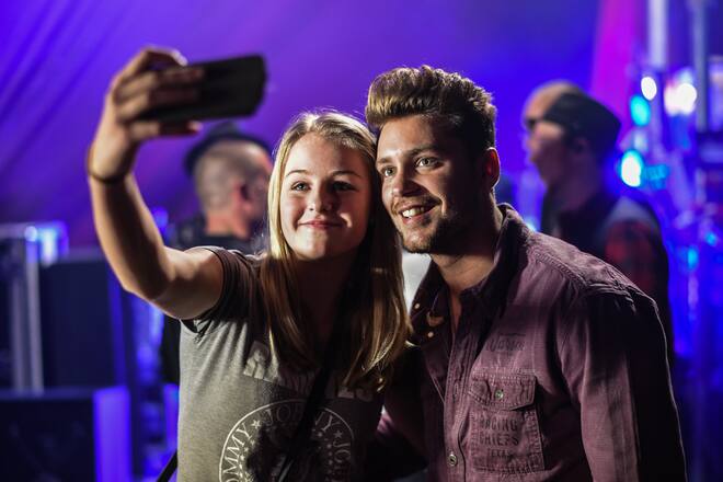Eine glückliche junge Frau wurde ausgewählt, um Backstage mit Bastian Baker mit der PostCard Creator App ein Selfie zu machen, das ihr danach als Postkarte zugeschickt wird.