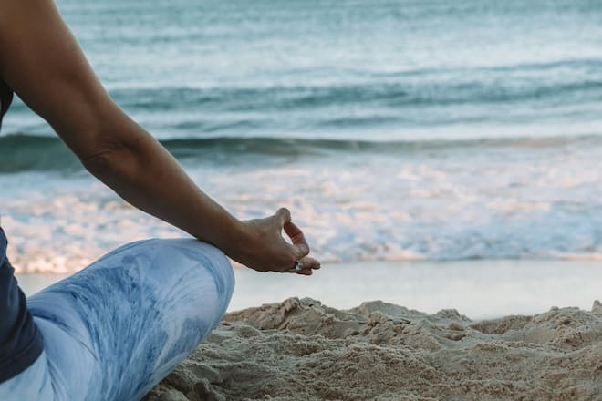 Frau von hinten, die Yoga am Strand macht.